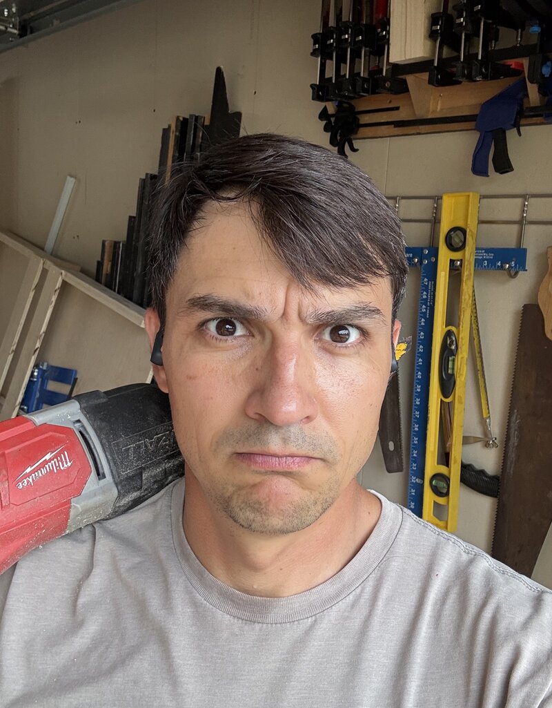 Dmitri Kochelorov in his garage workshop, a reciprocating saw resting on his shoulder